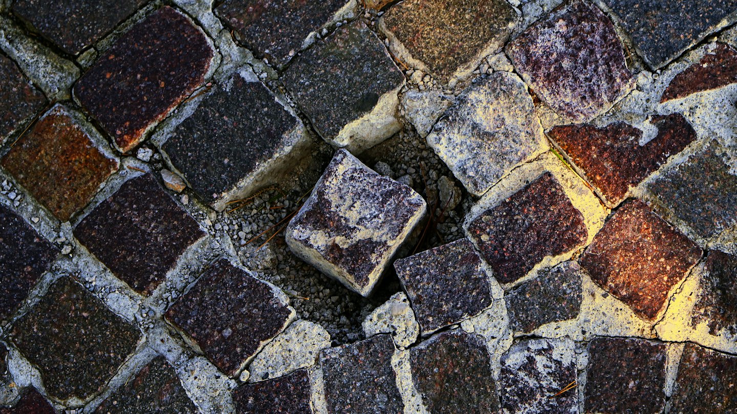 Odkruszony kamień odsłaniający żwir pod znoszoną brukową nawierzchnią.